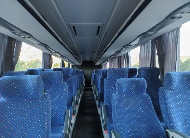 A bus interior with rows of blue seats, overhead compartments, and windows. 3