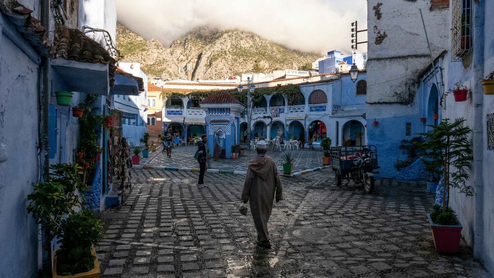 A cobblestone street with buildings painted in blue and white, a statue, and a mountain in the background. 5