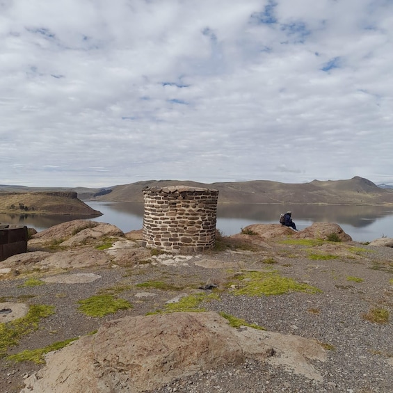 A stone structure near a lake with a person sitting on a rock in the background. 5