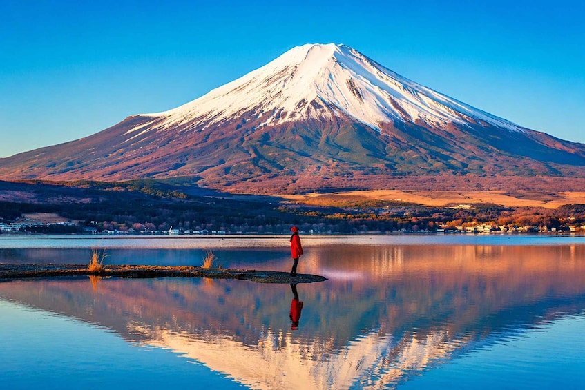 A snow-capped mountain, a calm lake, and a person in red. 5