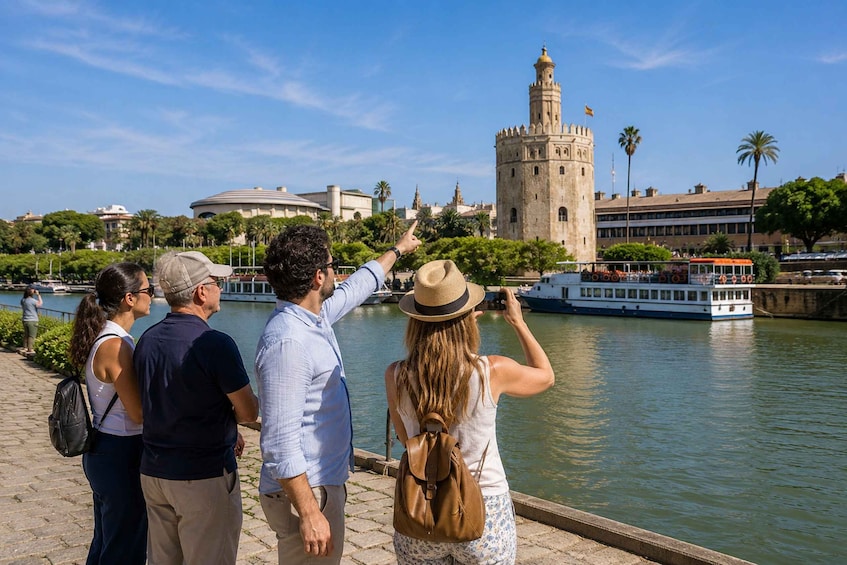 A group of people sightseeing along a riverside promenade, with a historic tower and a boat in the background. 1