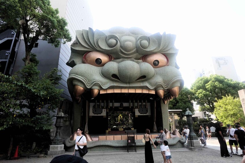A large stone statue of a mythical creature's face, a traditional building, and a crowd of people. 1