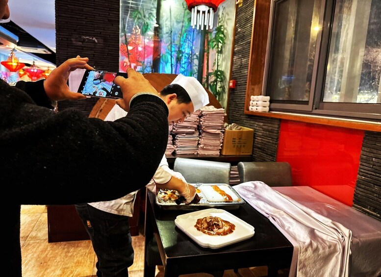 A person taking a photo of another person preparing food in a restaurant. 4