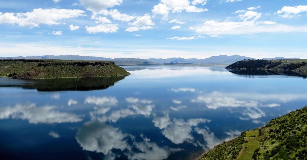A calm lake with a clear reflection of the sky and surrounding hills. 5