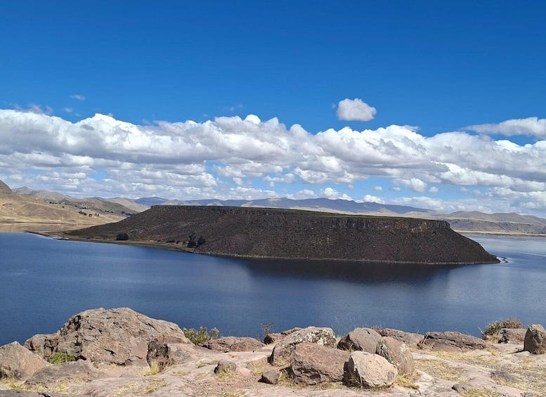 A large lake with a rocky shoreline and distant mountains under a partly cloudy sky. 4
