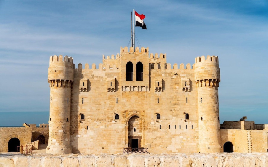 A historic stone castle with a flag, arched windows, and a central entrance. 4