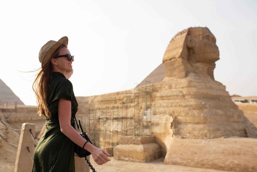 A person in a green dress and straw hat standing in front of the Great Sphinx. 3