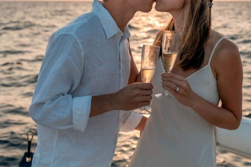 A couple holding champagne glasses on a boat with a body of water in the background. 3