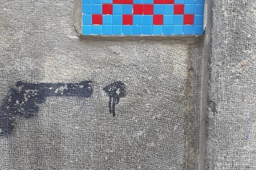 A wall with a red and blue mosaic tile pattern and a black graffiti mark. 3