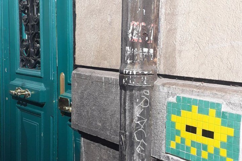A teal door with a metal grille, a concrete wall with graffiti, and a pixelated yellow and green pattern. 2