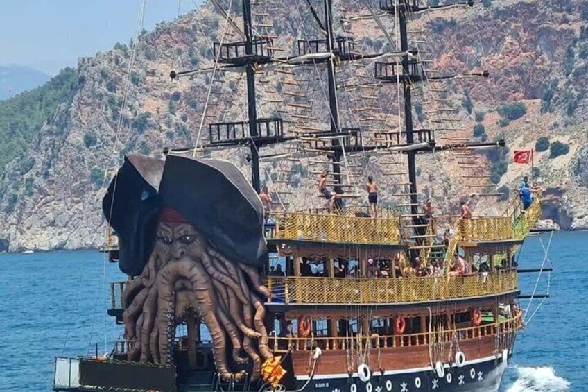 A ship with a large octopus sculpture on the bow, sailing near rocky cliffs. 1