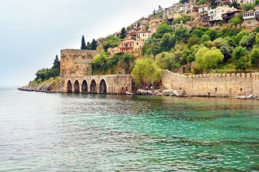A coastal cityscape with a historic fortification, clear turquoise waters, and terraced buildings. 2