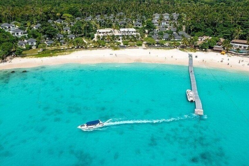 Una barca su acqua turchese, un pontile che si protende verso il mare e una spiaggia con edifici sullo sfondo. 3