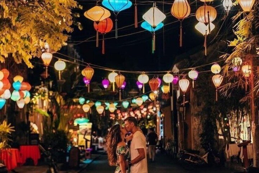 Una coppia si abbraccia sotto lanterne colorate in un ambiente esterno poco illuminato. 5