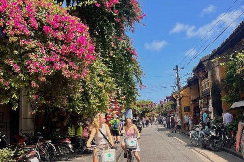 Calle bordeada de edificios, bicicletas y flores de buganvilla rosadas. 2