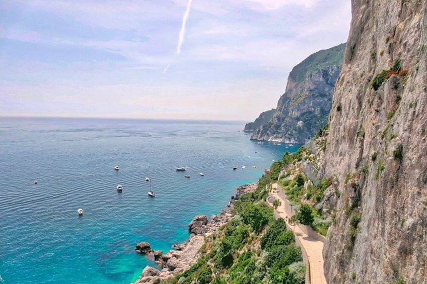 A coastal landscape with a winding road, clear blue sea, and rocky cliffs. 1