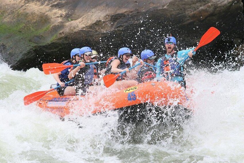 Eine Gruppe von Menschen in einem orangenen Schlauchboot durchfährt tosendes Weißwasser. 1