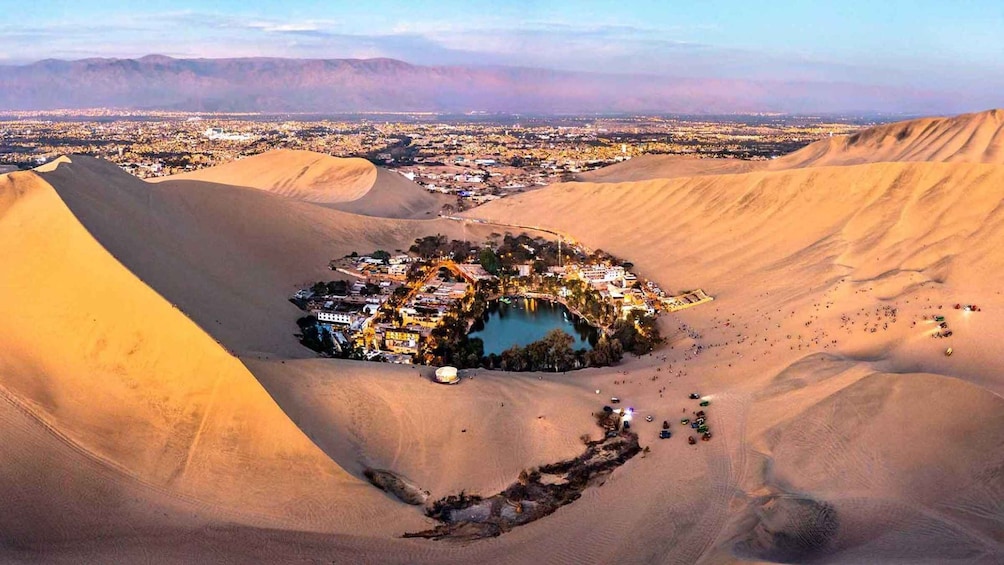 A desert landscape with sand dunes and a small settlement with a central water body. 1
