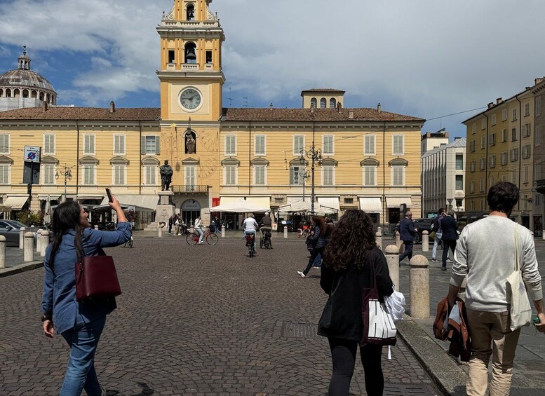 A square with a clock tower, cobblestone pavement, and people walking and cycling. 5