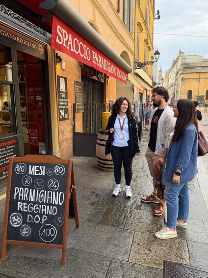 A street with a restaurant named 'SPACCO PARMIGIANO REGGIANO' and a chalkboard sign listing prices for dishes. 2