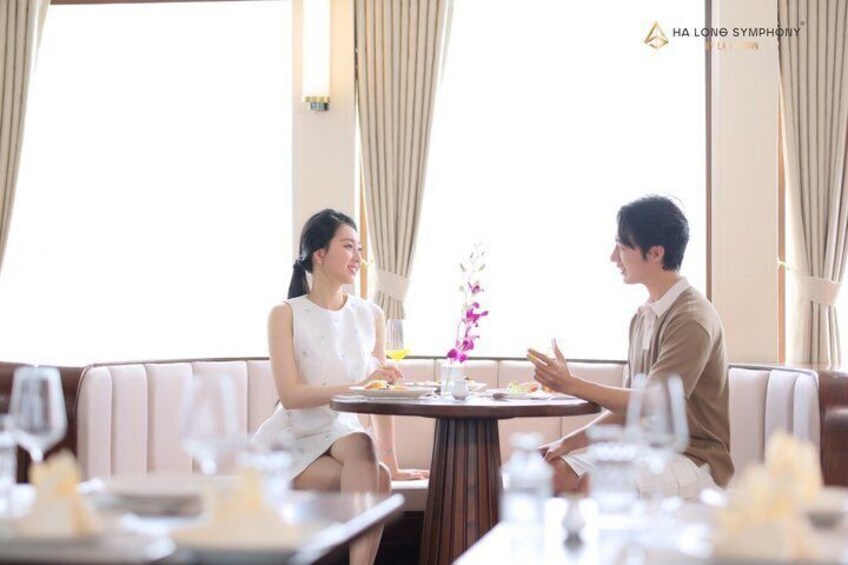 Una pareja cenando en un restaurante moderno con una mesa para dos, un jarrón de flores y vistas de la ciudad. 3