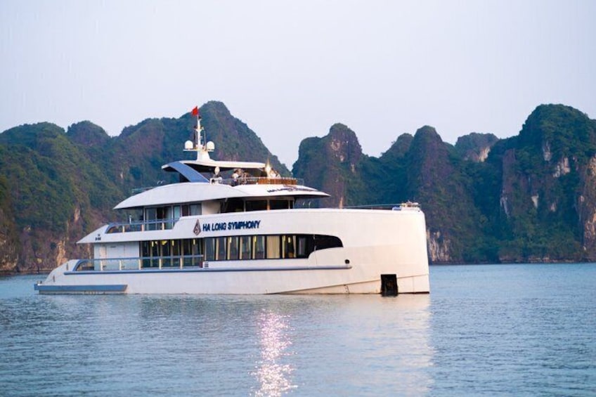 Un yate blanco grande llamado 'HA LONG SYMPHONY' sobre aguas tranquilas, con una costa montañosa al fondo. 1