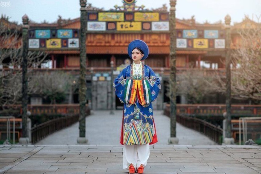 A person in traditional attire standing in front of a building with a tiled roof and colorful signage. 1