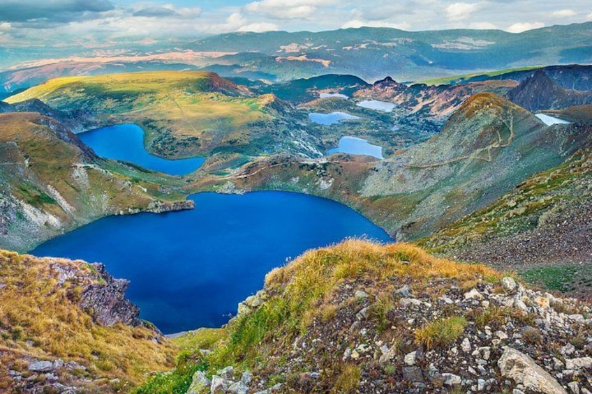 Eine gebirgige Landschaft mit einem großen, blauen See, umgeben von felsigem Gelände und weit entfernten Hügeln. 1