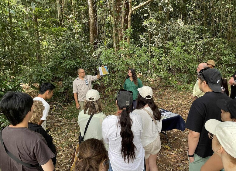 A group of people in a forested area, some standing and others seated, with a table and a person holding a map. 5