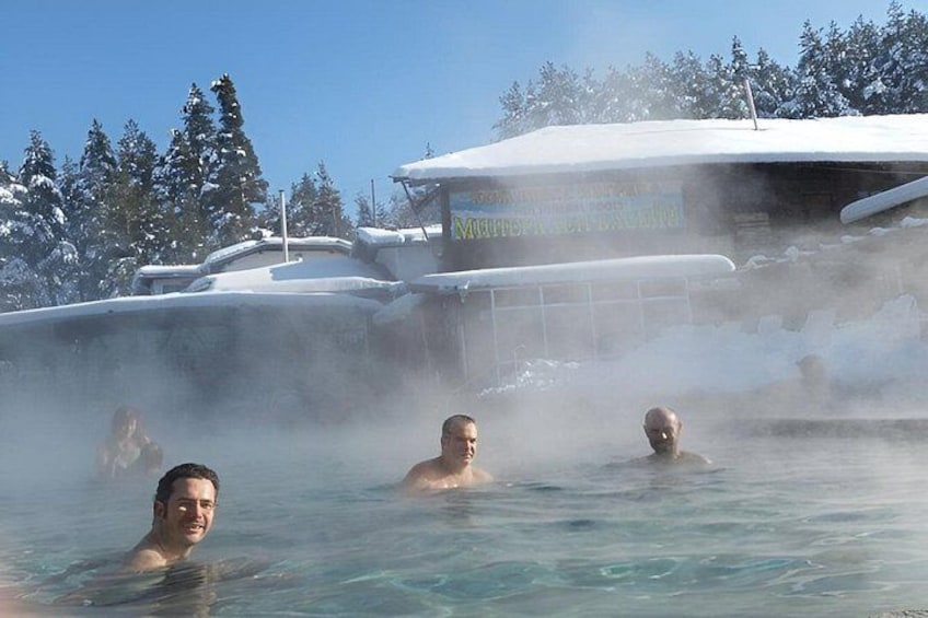 A hot spring with steam rising, surrounded by snow-covered trees and a building. 4