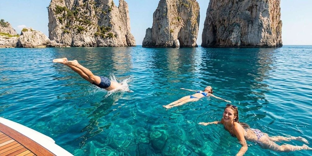 Two people floating in a clear blue sea with rocky cliffs in the background. 5