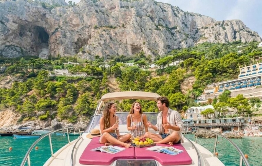 A boat with three people sitting on the deck, a rocky coastline, and a building with blue windows in the background. 3