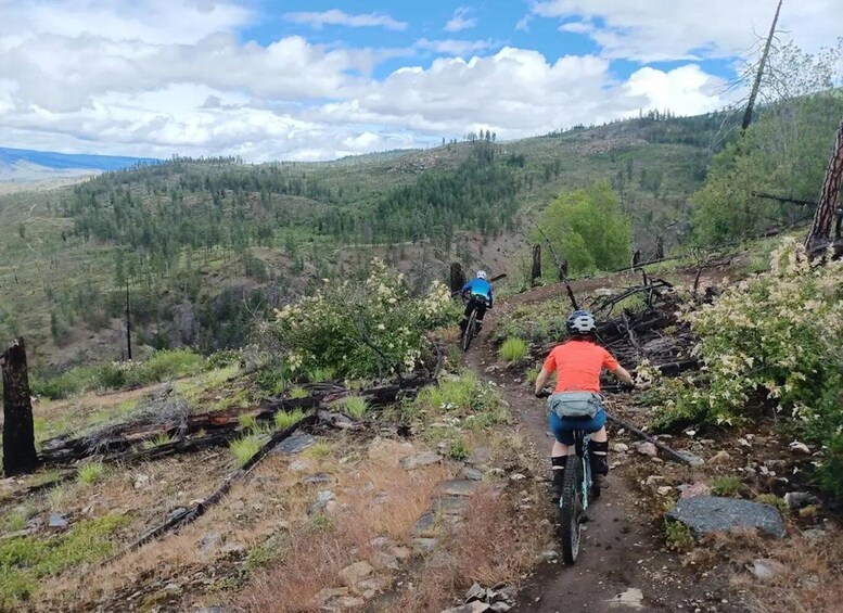 Two mountain bikers on a dirt trail surrounded by forested hills. 1