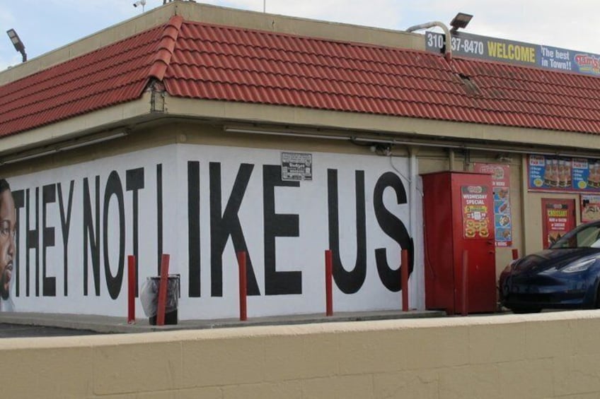 Un edificio con un cartel que dice 'THEY NOT LIKE US' y una cabina telefónica roja. 3