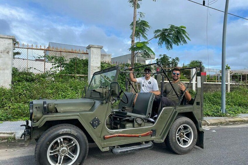En grön jeep står parkerad på en gata, med ett staket och palmer i bakgrunden. 2