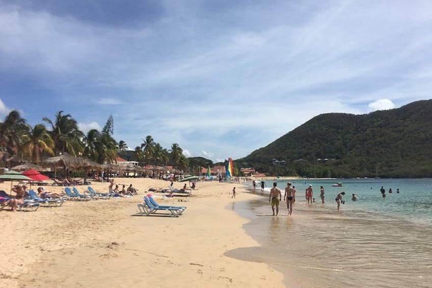 A beach with people walking and swimming, palm trees, and a mountain in the background. 2