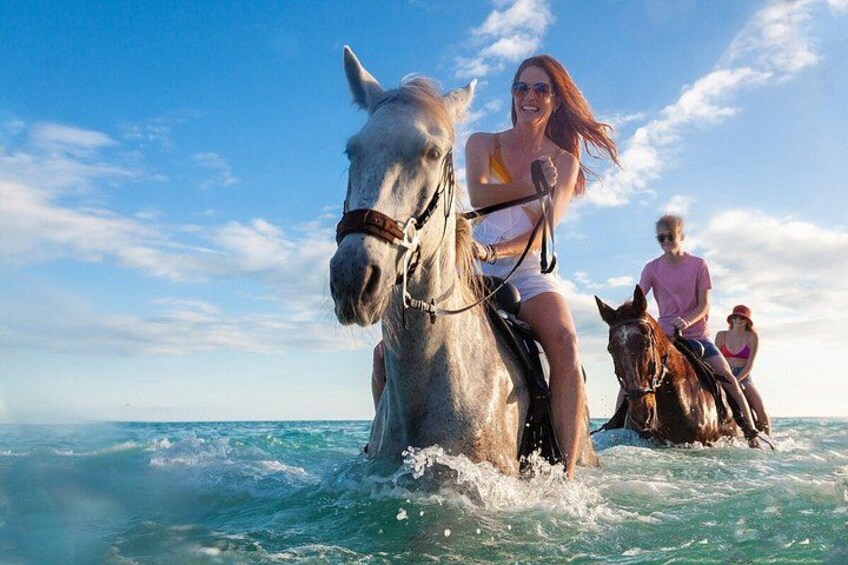 Two horses and riders on a body of water under a clear sky. 1