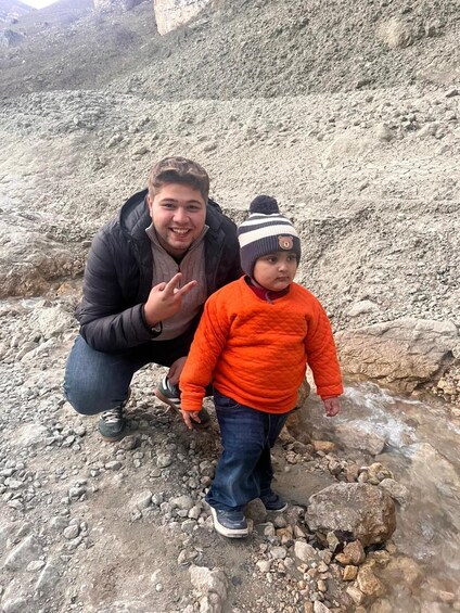 A person crouching next to a child on rocky terrain with a stream. 4