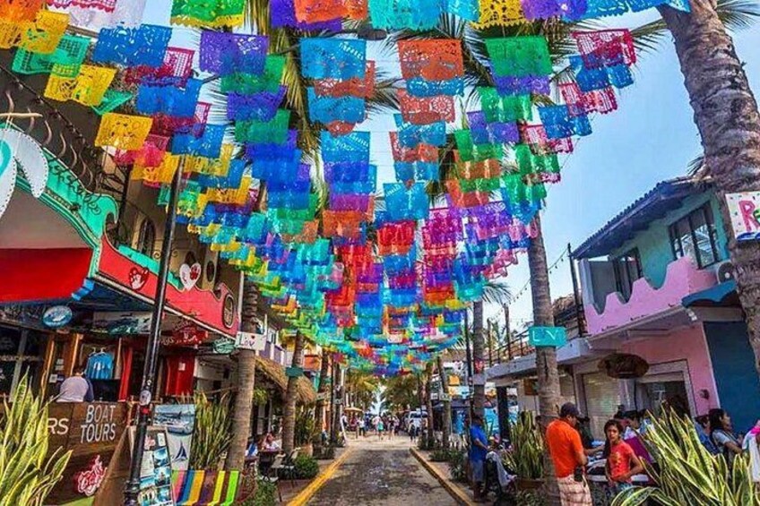 Una calle flanqueada por faroles de papel de colores, palmeras y diversas tiendas. 3
