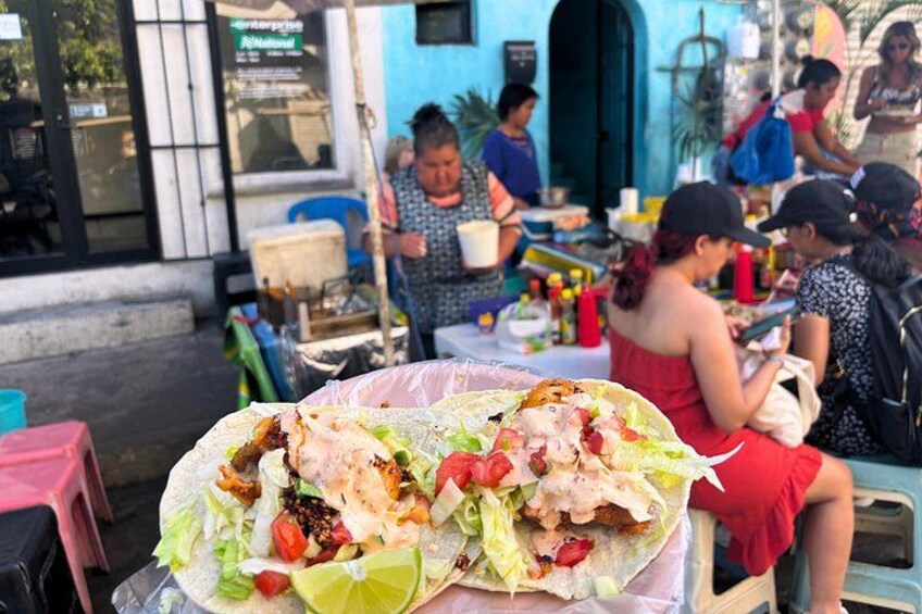 Puesto de comida callejera con tacos y un grupo de gente. 2