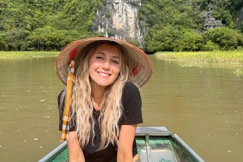 A person in a boat with a traditional conical hat, surrounded by calm water and greenery. 3