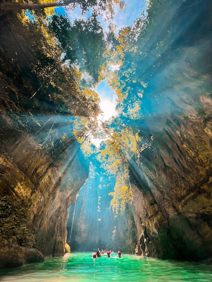 A cave with clear water, surrounded by trees and sunlight streaming through. 5