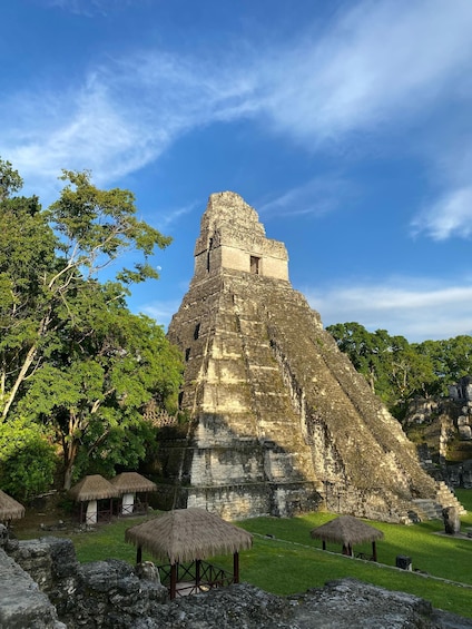 A large ancient pyramid with a small window, surrounded by lush greenery and thatched-roof huts. 3