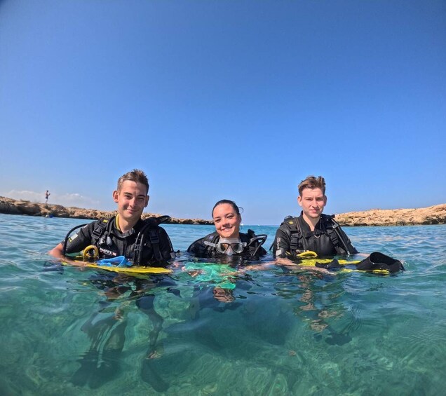 Three people in wetsuits holding diving boards in clear water with rocky shorelines. 5