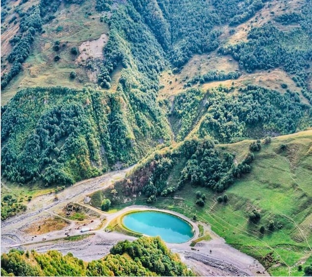 A mountainous landscape with a turquoise lake surrounded by dense forest. 3