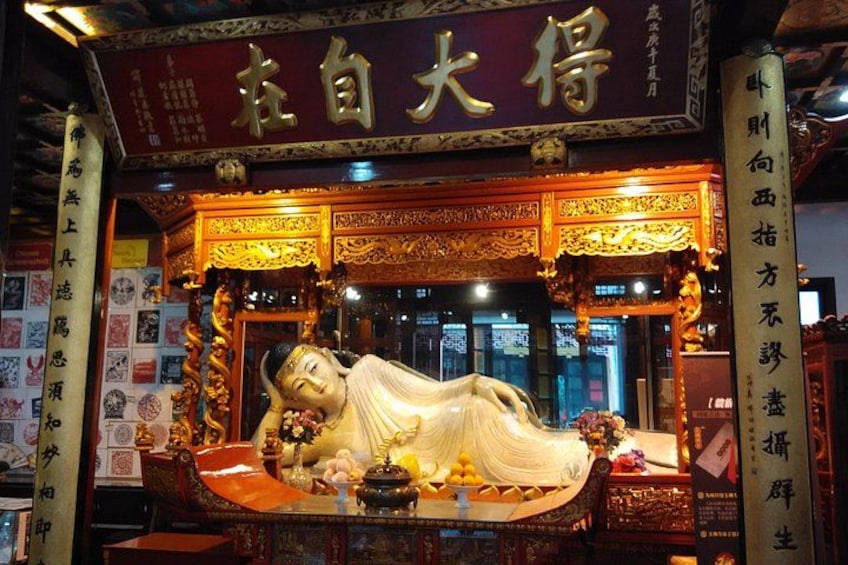 A statue of a reclining figure in a temple setting with ornate decorations and Chinese characters. 1
