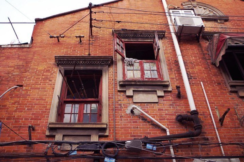 A red brick building with two windows, one with a broken pane, and exposed electrical wiring. 3