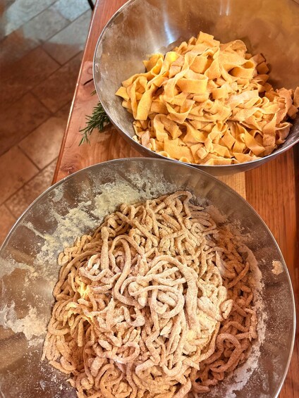 Twee metalen kommen op een houten tafel, één met pasta en de andere met een mengsel van bloem. 4