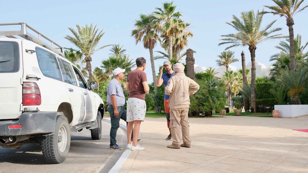 A group of people standing by a white SUV in a landscaped area with palm trees. 1