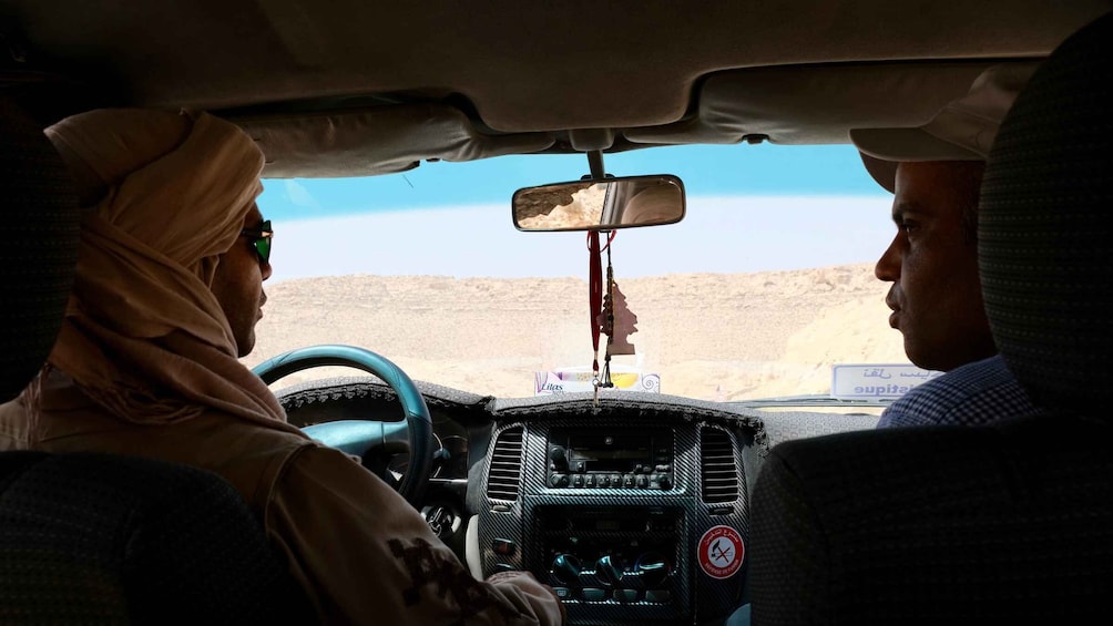 A desert landscape with a clear sky, a vehicle interior, and a driver wearing a headscarf. 2